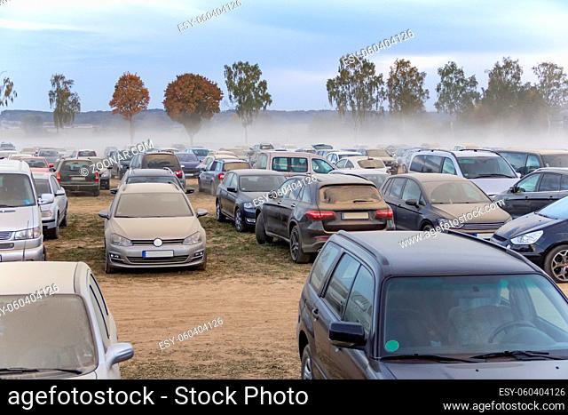 dusty parking space scenery on a field including lots of dust covered cars at evening time in Southern Germany