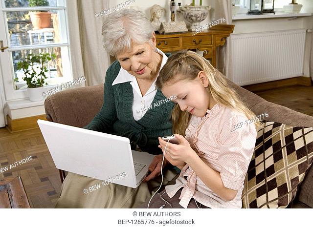 Old lady using laptop while spending time with her granddaugther