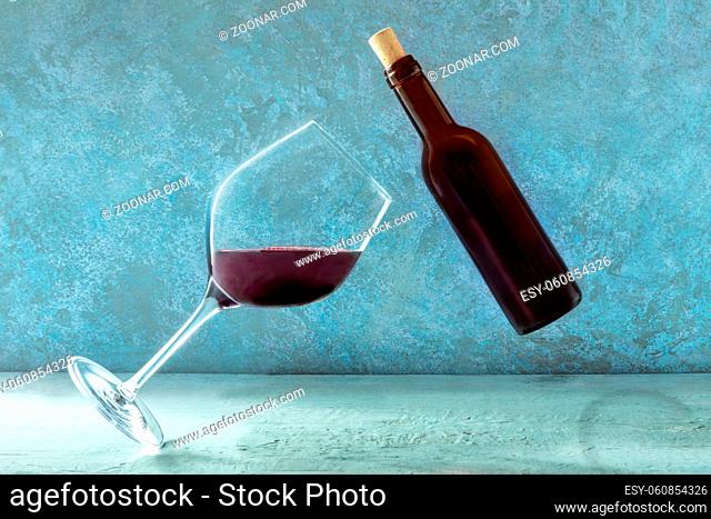 Red wine, a glass and a bottle, floating in mid-air against a blue background. Winetasting concept