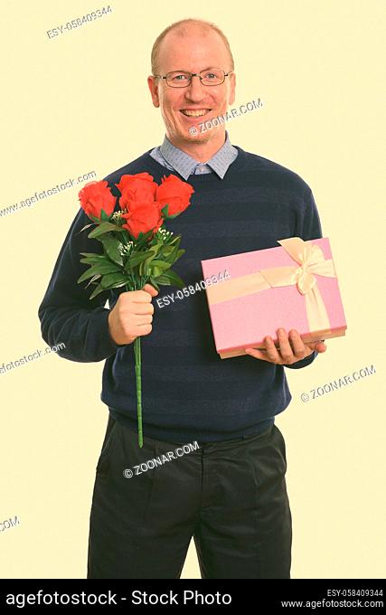 Studio shot of happy man smiling while holding red roses and gift box ready for Valentine's day