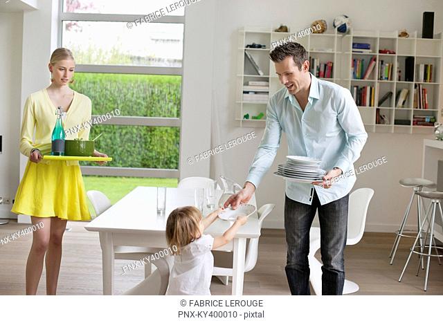 Woman serving food with her husband and daughter holding plates at dining table