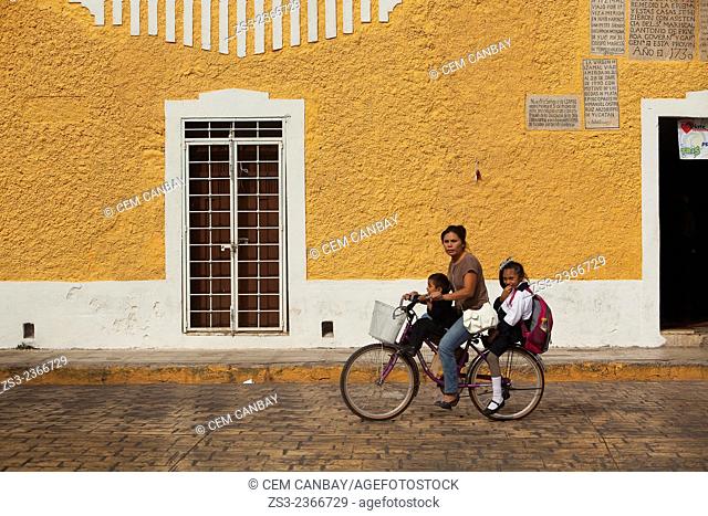 Woman riding on a bike with her children in the streets of the town, Izamal, Yucatan, Yucatan Province, Mexico, Central America