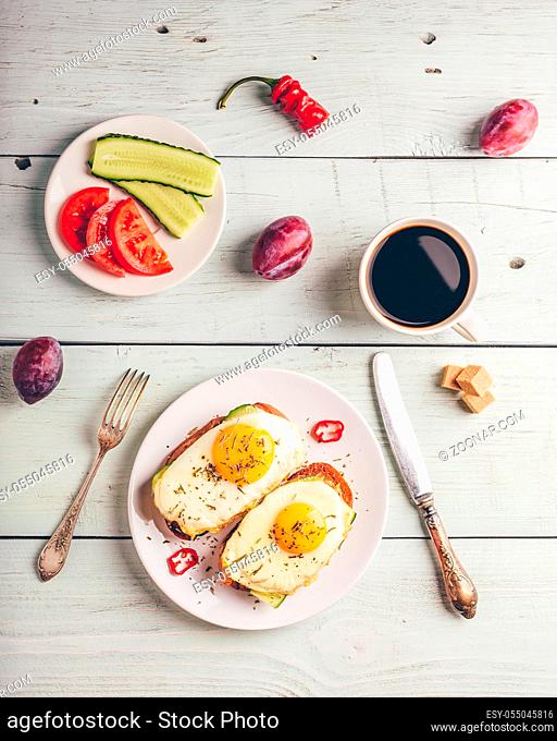 Breakfast toasts with vegetables and fried egg on white plate, cup of coffee and some fruits over wooden background. Clean eating food concept