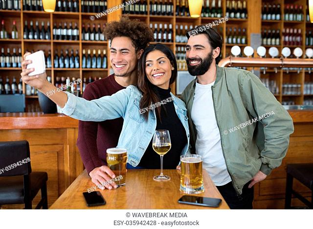 Friends taking selfie with mobile phone while having glass of beer