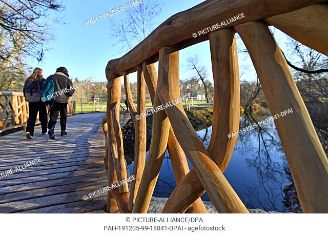 05 December 2019, Thuringia, Weimar: Walkers walk over the newly built natural bridge in the park at the Ilm. The predecessor building was severely damaged...
