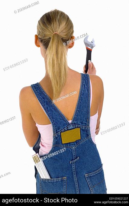 Young blonde wearing dungarees with spanner in hand and measure in pocket. Isolated on white in studio. Rear view
