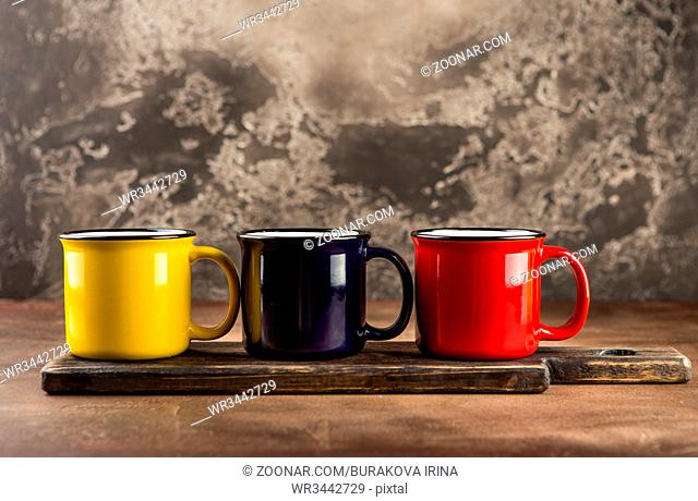 Colorful ceramic mugs with enamel look on wooden cutboard