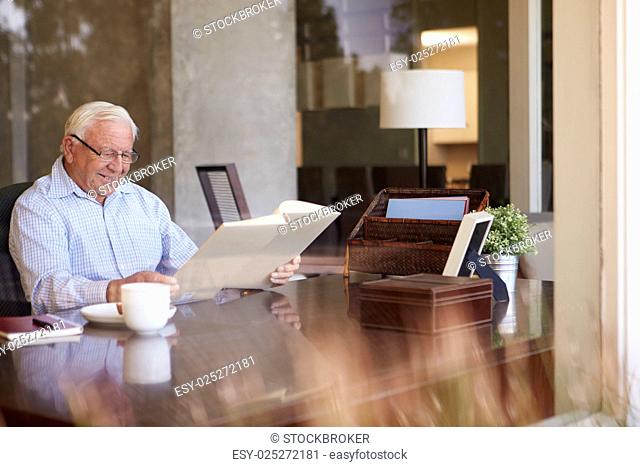 Senior Man Looking At Photo Album Through Window