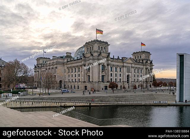 December 28, 2020, Berlin, the Reichstag building by master builder Paul Wallot on the Platz der Republik with flags on the day with cloudy skies
