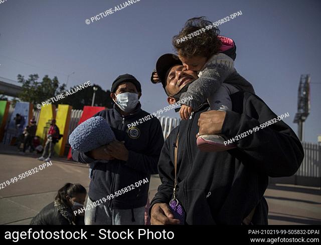 18 February 2021, Mexico, Tijuana: A man of Central American origin holds his son after protesting at the border crossing