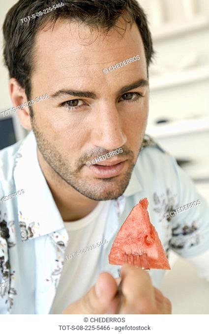 Portrait of a young man holding a slice of watermelon with a fork