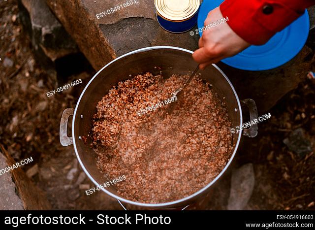 Camper preparing meal in large kettle on campfire from above