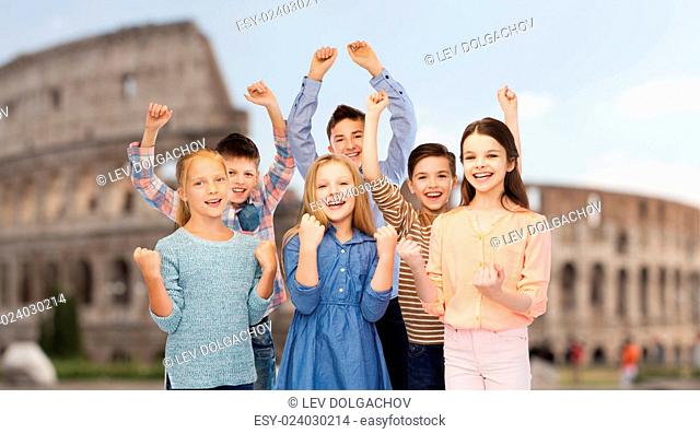childhood, travel, tourism, gesture and people concept - happy children friends raising fists and celebrating victory over coliseum in rome