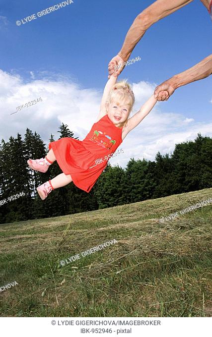 Blonde little girl being swung around, 2 years old, outside