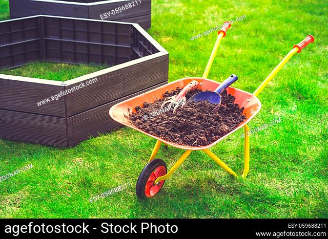 Garden barrow with soil and empty raised beds on grass prepared for filling with soil. Urban gardening concept