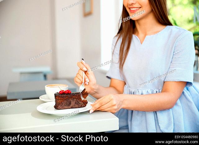 Young attractive Caucasian lady enjoy eating chocolate cake with hot coffee in modern coffee shop at noon