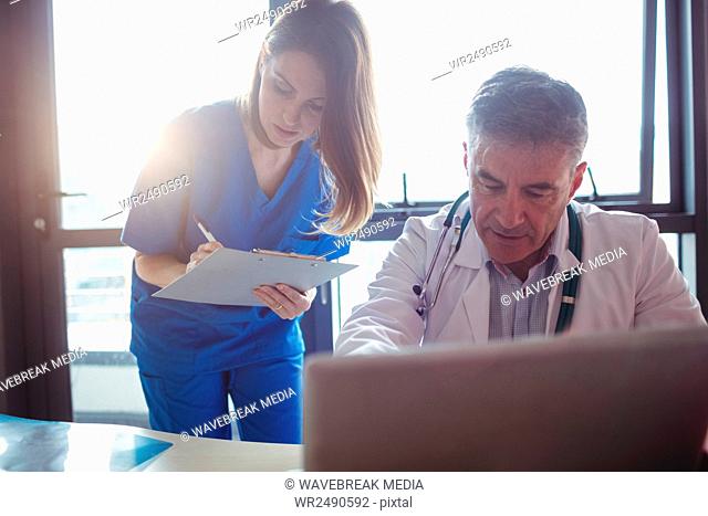 Doctor discussing with nurse over laptop