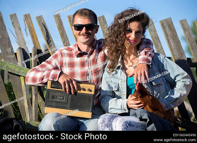A girl with a chicken and a man with a retro magnetophone are sitting on the bench. The villagers are in the style of the nineties