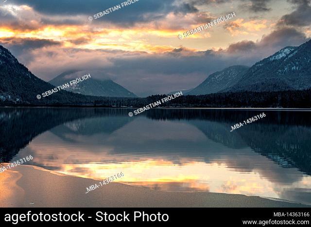 The colors of the sunset are reflected in the water and the beginning ice layer of the Sylvenstein reservoir, in the background the Karwendel mountains