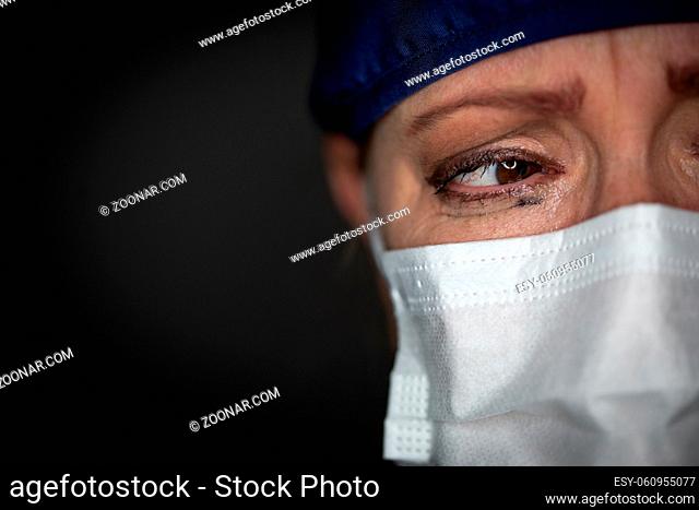 Tearful Stressed Female Doctor or Nurse Wearing Medical Face Mask on Dark Background