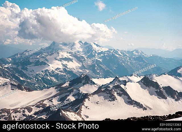 A dark blue sky with clouds on the rocky peaks of mountains covered with glaciers and snow in the Caucasus