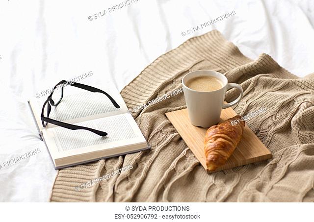coffee, croissant, blanket and book on bed at home