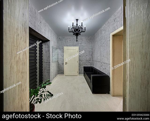 Hall in a modern style with concrete walls, a glowing lamp and light tiles on the floor. There is a door with blinds, a light door, a mirror