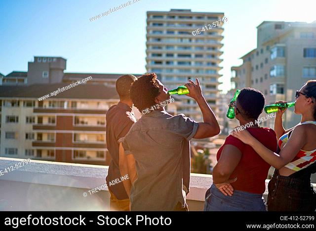 Young friends drinking beer on sunny urban rooftop