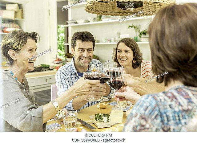 Adult friends making a toast with red wine at dining table