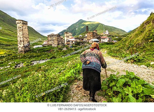 Old woman walking next to the koshki medieval towers of Ushguli, Georgia, the highest permanently inhabited village in Europe