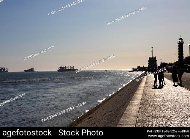 PRODUCTION - 06 April 2023, Portugal, Lissabon: Day trippers walk along the banks of the Tagus River in the Belem district in the early evening
