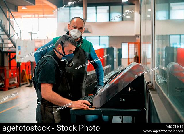 two workers wearing a face mask due to a coronavirus pandemic are programming a modern CNC machine. High quality photo