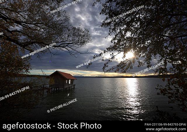 06 November 2023, Bavaria, Inning: The windows of a boathouse on Lake Ammersee reflect the sun's rays shining through a gap in the clouds