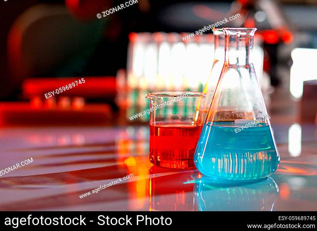 Illuminated laboratory flask filed with colorful chemical solutions with shadows on the table. Laboratory, science, reaserch, chemistry... consept