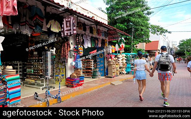 06 December 2023, Mexico, Playa del Carmen: Holidaymakers stroll past souvenir stores on ""Quinta Avenida"" (Fifth Avenue) in the center of the resort