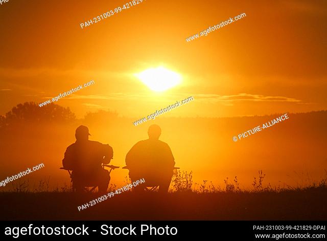 03 October 2023, Baden-Württemberg, Riedlingen: Two anglers sitting on camping chairs watching the sunrise Photo: Thomas Warnack/dpa