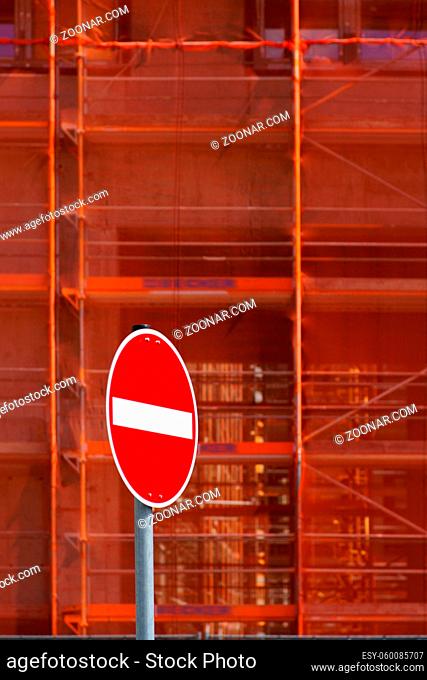 Die Nahaufnahme eines Baugerüstes mit Stützpfeilern und Auffangnetzen vor dem ein rotes Einbahnstraßenschild steht