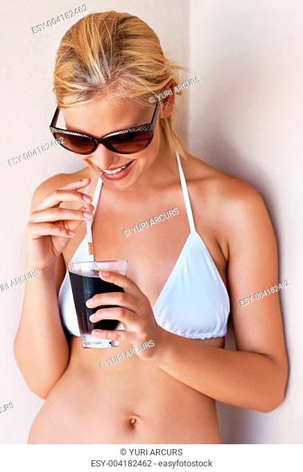 Happy young woman wearing a bikini enjoying a glass of cold drink