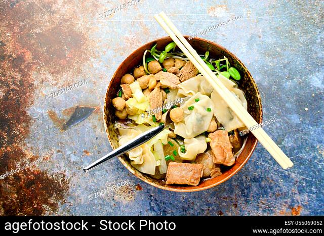 Wonton soup with meat balls, spring onion served in a big brown bowl, selective focus