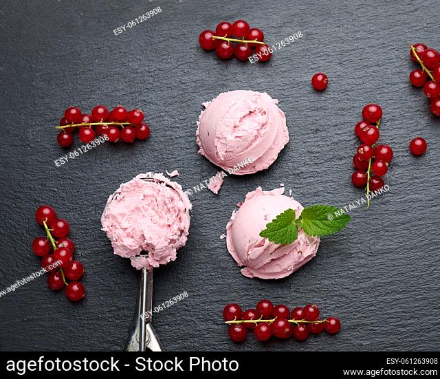 Pink ice cream balls on a black stone board, red currant berries nearby, top view
