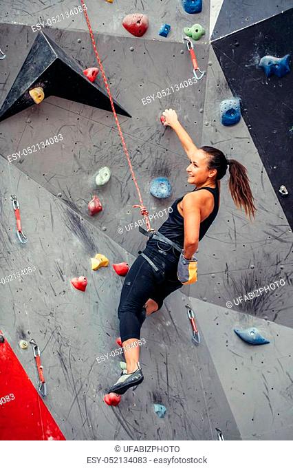 Sporty strong young woman in black outfit exercising in boulder climbing hall reaching new results, enjoying new challenges