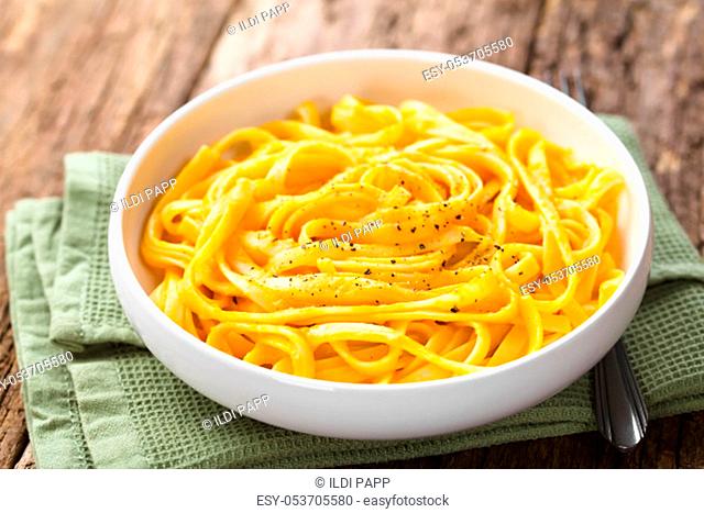 Fettuccine pasta with fresh homemade creamy pumpkin alfredo sauce garnished with freshly ground black pepper and served in bowl (Selective Focus