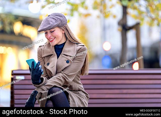 Beautiful woman using phone while sitting on bench in park