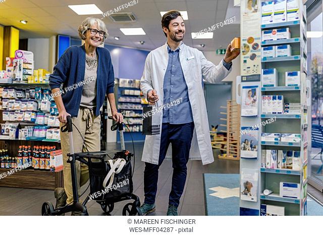 Smiling pharmacist and customer with wheeled walker in pharmacy