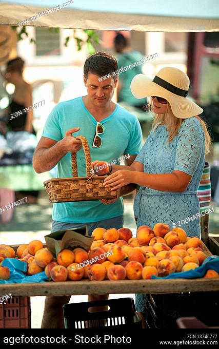 A young couple with a basket chooses peaches at the counter