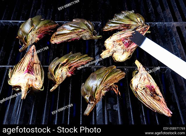 Grilled Artichokes: Tongs turning an artichoke half on a gas grill