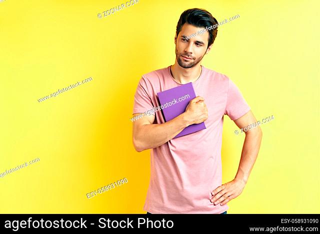 Portrait of young handsome man with book on yellow background
