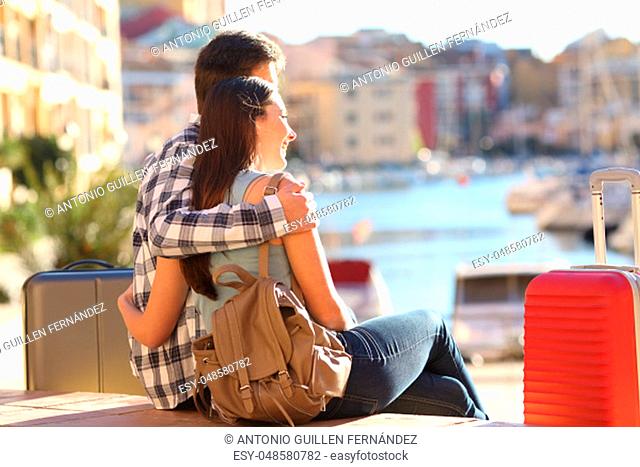 Couple of tourists sitting and cuddling while watching vacations destination in a port with colorful urban buildings in the background