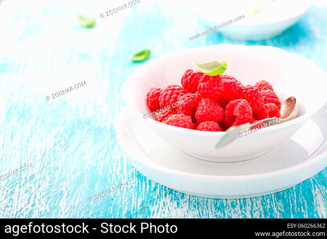 Fresh raspberries in a white ceramic bowl with metal spoon. closeup, selective focus
