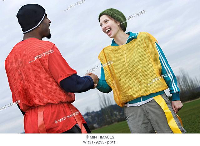 Black man and Caucasian woman team members shaking hands at a sporting event